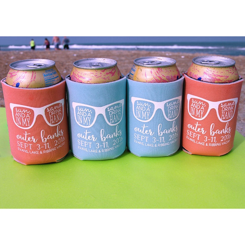 K&ouml;nnte beinhalten: Vier bunte Getr&auml;nkedosenk&uuml;hler mit dem Text "sun and a drink in my hand" und "outer banks sept 3-11, 2016" darauf gedruckt. Die K&uuml;hler stehen in einer Reihe auf einer gr&uuml;nen Oberfl&auml;che.