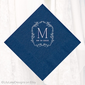 Puede incluir: Una servilleta cuadrada azul marino con un dise&ntilde;o de corona floral blanca. La corona rodea la letra "M" y la fecha "08.14.2025". La servilleta est&aacute; hecha de un material texturizado, ideal para una boda o evento especial.