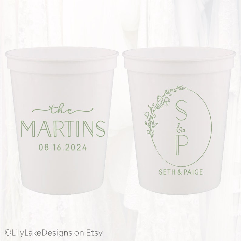May include: Two white plastic cups with green text and designs. One cup says "the MARTINS 08.16.2024" and the other cup has a circle with the letters "S&P" and a floral design around the circle. The text below the circle says "SETH & PAIGE".