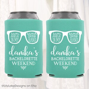 K&ouml;nnte beinhalten: Zwei t&uuml;rkisblaue Getr&auml;nkedosenk&uuml;hler mit wei&szlig;em Text und einer Grafik von Sonnenbrillen. Der Text lautet "sun, and a in my, sand drink hand" und "danika's bachelorette weekend".