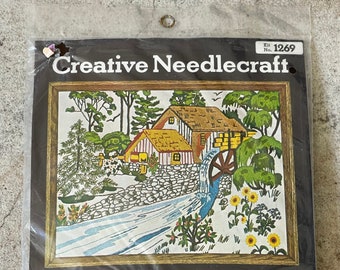 May include: A needlepoint kit featuring a colorful image of a water wheel and a cottage with a thatched roof. The kit includes a 17x21 inch panel, yarn, needle, and instructions. The kit is labeled "Water Wheel" and "Sultana The Quality Line".