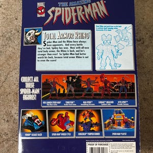 Puede incluir: La parte trasera de un paquete de figuras de acci&oacute;n vintage de Spider-Man. El paquete presenta el texto "Total Armor Rhino" e im&aacute;genes de otras figuras y juegos de Spider-Man. El logotipo de Marvel es visible.