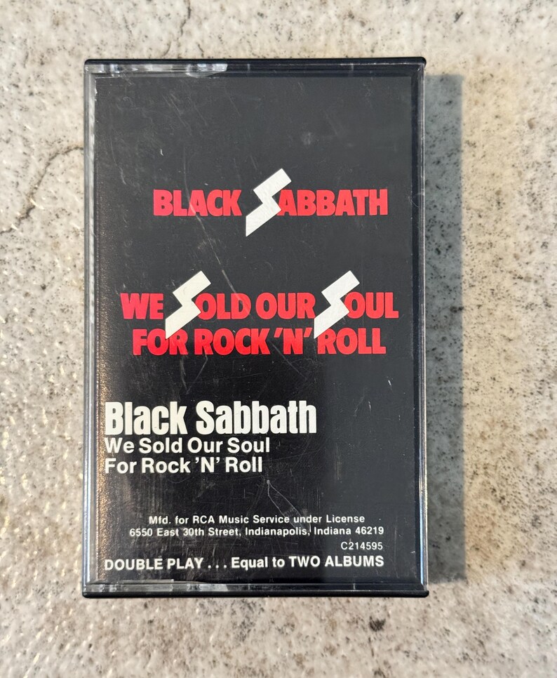 May include: A Black Sabbath cassette tape with a black case. The band's name and album title, "We Sold Our Soul For Rock 'N' Roll", are displayed in red and white. The text "DOUBLE PLAY... Equal to TWO ALBUMS" is also visible on the cassette.