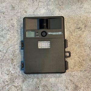 May include: A black Wildview trail camera with a rectangular shape. The camera has a lens, flash, and a small LCD screen. The text "Wildview" is printed on the top of the camera. The camera is designed for outdoor use.