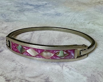May include: A silver bangle bracelet with a pink and white inlay of mother of pearl. The bracelet has a hinged clasp.