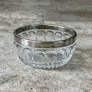 K&ouml;nnte beinhalten: Eine klare Glassch&uuml;ssel mit silbernem Rand. Die Sch&uuml;ssel hat ein dekoratives Muster aus kleinen Kreisen.