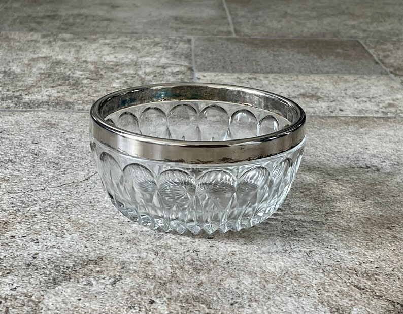 K&ouml;nnte beinhalten: Eine klare Glassch&uuml;ssel mit silbernem Rand. Die Sch&uuml;ssel hat ein dekoratives Muster aus kleinen Kreisen.