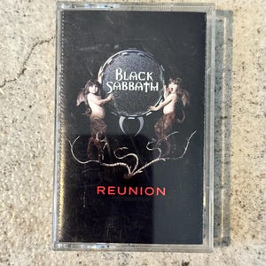 May include: Black Sabbath "Reunion" cassette tape. The cassette case is transparent, with a black cover featuring the band's logo and album title. The cover art includes two figures and the word "REUNION" in red.