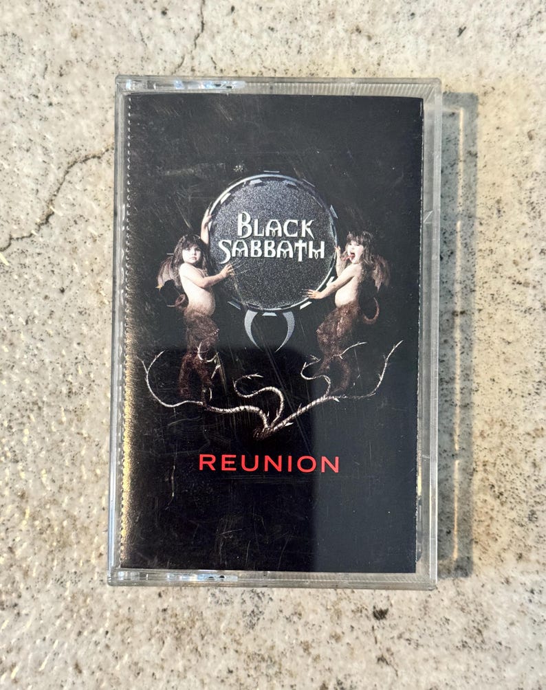 May include: Black Sabbath "Reunion" cassette tape. The cassette case is transparent, with a black cover featuring the band's logo and album title. The cover art includes two figures and the word "REUNION" in red.