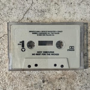 May include: A retro cassette tape for Ozzy Osbourne's album "No Rest for the Wicked." The tape is in a clear plastic case and features the album title and song titles such as "Miracle Man" and "Devil's Daughter." The cassette is labeled "Side 1."