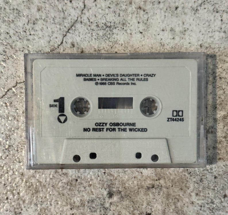 May include: A retro cassette tape for Ozzy Osbourne's album "No Rest for the Wicked." The tape is in a clear plastic case and features the album title and song titles such as "Miracle Man" and "Devil's Daughter." The cassette is labeled "Side 1."