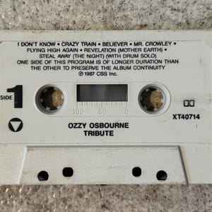 May include: A white cassette tape featuring the album "Ozzy Osbourne Tribute." The tape lists song titles including "Crazy Train" and "Believer." It has a "Side 1" marker and the text "1987 CBS Inc."