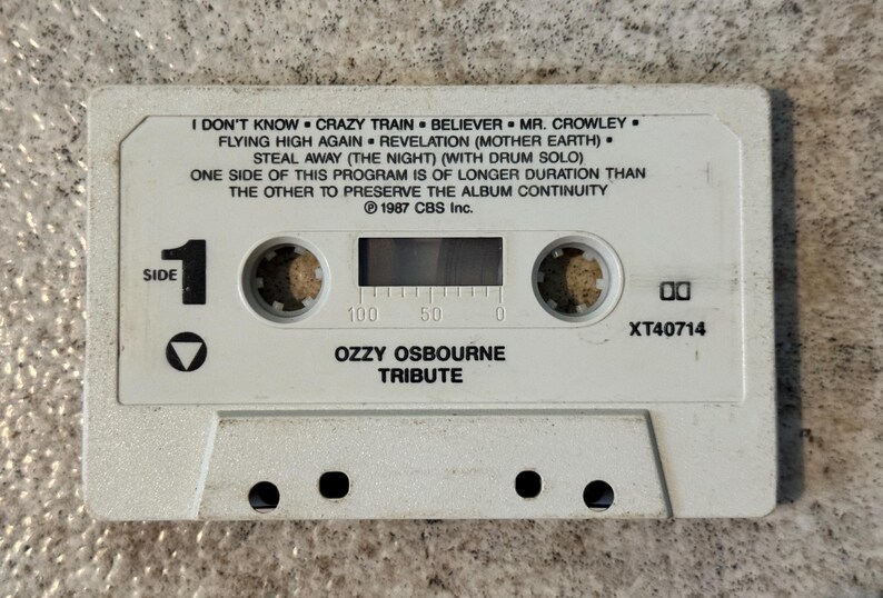 May include: A white cassette tape featuring the album "Ozzy Osbourne Tribute." The tape lists song titles including "Crazy Train" and "Believer." It has a "Side 1" marker and the text "1987 CBS Inc."
