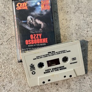 May include: A vintage cassette tape of Ozzy Osbourne's "Bark at the Moon" album. The album cover features a monster illustration. The white cassette tape has the album title and artist's name printed on it. The cassette case is black.