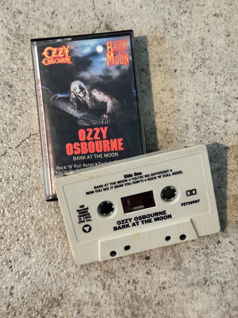 May include: A vintage cassette tape of Ozzy Osbourne's "Bark at the Moon" album. The album cover features a monster illustration. The white cassette tape has the album title and artist's name printed on it. The cassette case is black.