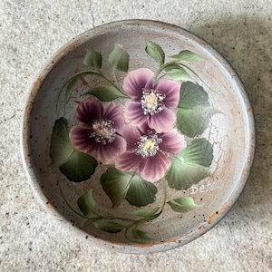 May include: A round, hand-painted bowl with a floral design. The bowl features three purple flowers with yellow centers and green leaves. The bowl has a distressed, crackled finish and is approximately 8 inches in diameter.
