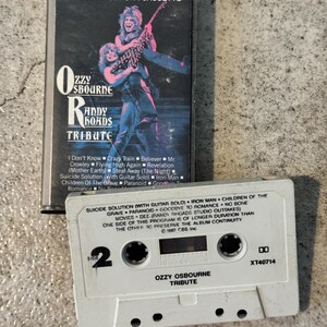 May include: A vintage cassette tape and case for the Ozzy Osbourne Randy Rhoads Tribute album. The case features a graphic of two musicians. The cassette tape is white with the album title and track listing.