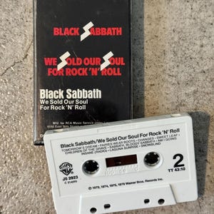 May include: A vintage cassette tape and case for Black Sabbath's album "We Sold Our Soul For Rock 'N' Roll." The black case features white text and a lightning bolt. The white cassette tape displays the album title and track list.