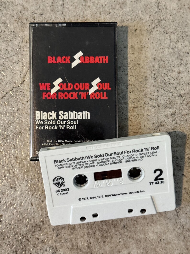 May include: A vintage cassette tape and case for Black Sabbath's album "We Sold Our Soul For Rock 'N' Roll." The black case features white text and a lightning bolt. The white cassette tape displays the album title and track list.