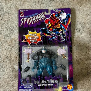 Puede incluir: Figura de acci&oacute;n sellada de Total Armor Rhino de la serie Spider-Man Special Collector. La figura es azul con armadura gris y viene con dos armas en forma de martillo. El embalaje presenta ilustraciones de Spider-Man y el logotipo de Toy Biz.
