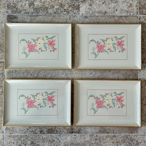 May include: Four framed floral prints. Each print features a light green background with a gold border. The floral design includes pink, white, and green elements. The frames are rectangular and have a gold trim.
