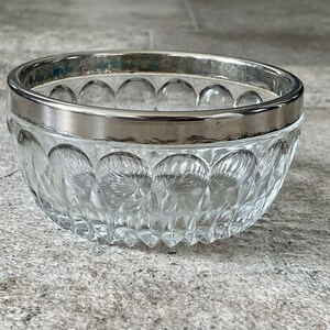 K&ouml;nnte beinhalten: Eine klare Glassch&uuml;ssel mit silbernem Rand. Die Sch&uuml;ssel hat ein dekoratives Muster aus kleinen, erhabenen Kreisen.