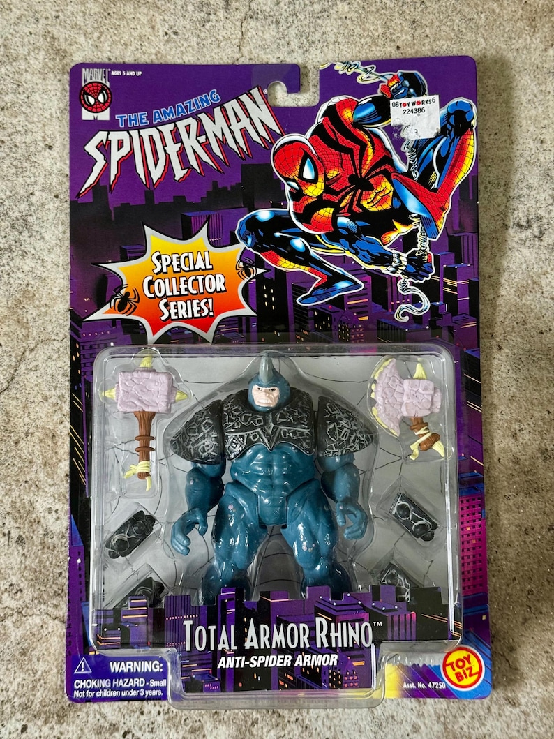 Puede incluir: Figura de acci&oacute;n Total Armor Rhino de la serie Special Collector, empaquetada en una tarjeta morada con gr&aacute;ficos de Spider-Man. La figura de Rhino es azul con armadura gris y accesorios. El embalaje incluye una advertencia sobre peligro de asfixia.