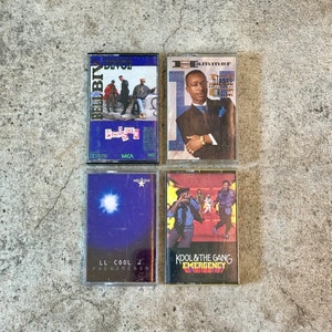 May include: Four cassette tapes with different album covers. The top left tape is blue and white with the text "DEVOE" and "Poison" in red. The top right tape is blue and white with the text "Hammer" and "Please Hurt Me" in red. The bottom left tape is blue with a white star and the text "LL COOL J" and "PHENOMENON". The bottom right tape is red and white with the text "KOOL & THE GANG" and "EMERGENCY".