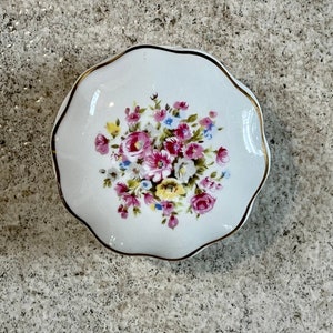 Op de afbeelding: Een wit porseleinen sieradenbakje met een gouden rand en een bloemmotief met roze, gele en blauwe bloemen.