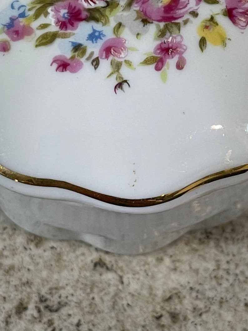 Op de afbeelding: Wit porseleinen sieraden doosje met een gouden rand en een bloemenontwerp met roze, gele en blauwe bloemen.