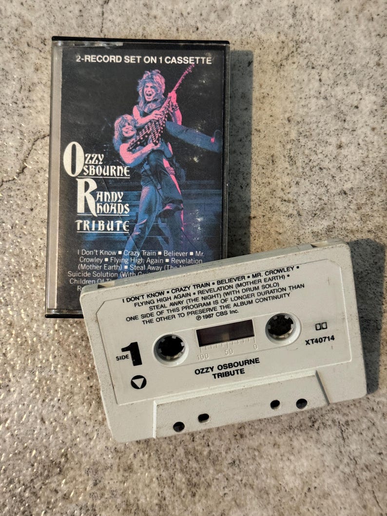 May include: A vintage cassette tape of the Ozzy Osbourne Randy Rhoads Tribute album. The cassette case features a colourful image of the musicians. The white cassette tape has the album title and song list printed on it. The album was released in 1987.