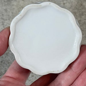 Op de afbeelding: Witte keramische sieraden schaal met een gegolfde rand. De schaal is rond en heeft een gladde, glanzende afwerking.