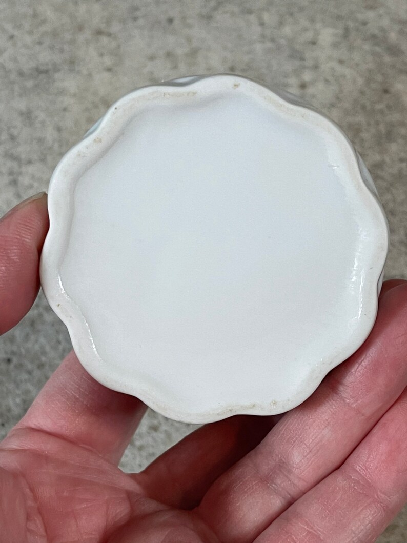 Op de afbeelding: Witte keramische sieraden schaal met een gegolfde rand. De schaal is rond en heeft een gladde, glanzende afwerking.