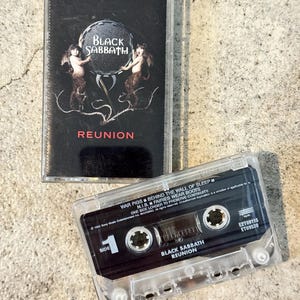 May include: Two vintage Black Sabbath "Reunion" cassette tapes. The cassette cases are clear, and the labels are black. The album cover features the band's name and the word "Reunion" in white text, with a graphic of two figures.