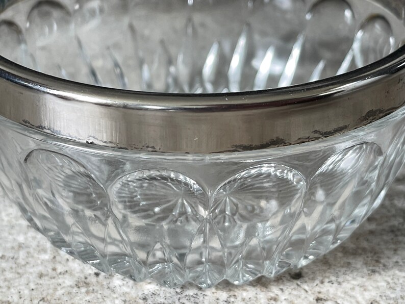 K&ouml;nnte beinhalten: Eine klare Glassch&uuml;ssel mit silbernem Rand. Die Sch&uuml;ssel hat ein dekoratives Muster aus kleinen, erhabenen Kreisen.