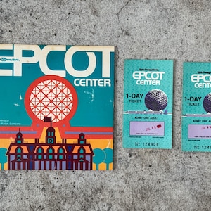 May include: Vintage EPCOT Center memorabilia, including a brochure and two 1-Day tickets. The brochure features the EPCOT Center logo with a geometric sphere and architectural elements. The tickets are teal with a sphere graphic.