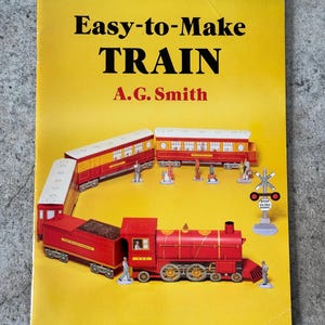 May include: A yellow book cover with the title "Easy-to-Make TRAIN" in black and red text. The cover features a red and yellow toy train set with miniature figures and a railroad crossing sign.