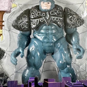 Puede incluir: Figura de acci&oacute;n azul de un personaje musculoso con un cuerno en la cabeza y armadura en los hombros. La figura est&aacute; en un paquete de pl&aacute;stico transparente con las palabras "TOTAL ARMOR RHINO" en la parte inferior.