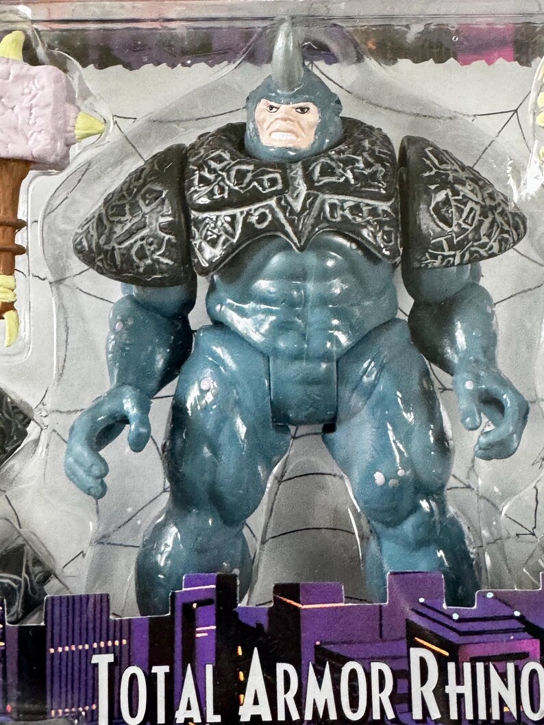 Puede incluir: Figura de acci&oacute;n azul de un personaje musculoso con un cuerno en la cabeza y armadura en los hombros. La figura est&aacute; en un paquete de pl&aacute;stico transparente con las palabras "TOTAL ARMOR RHINO" en la parte inferior.