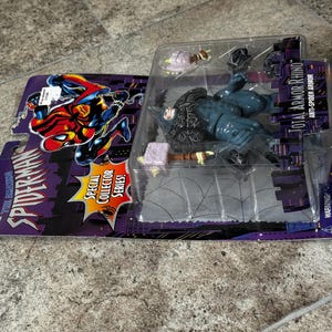 Puede incluir: Figura de acci&oacute;n de Spider-Man, "Total Armor Rhino", en un embalaje de pl&aacute;stico transparente. El embalaje es morado y negro, con las palabras "The Amazing Spider-Man" y "Special Collector Series!" impresas. La figura es azul y negra.