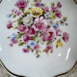 Op de afbeelding: Een witte porseleinen sieraden doosje met een gouden rand en een bloemenontwerp met roze, gele en blauwe bloemen.