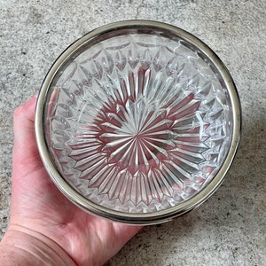 K&ouml;nnte beinhalten: Eine klare Glassch&uuml;ssel mit silbernem Rand und einem rautenf&ouml;rmigen Muster. Die Sch&uuml;ssel ist leer und hat eine reflektierende Oberfl&auml;che.