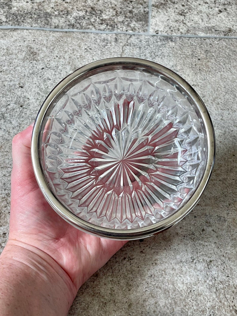 K&ouml;nnte beinhalten: Eine klare Glassch&uuml;ssel mit silbernem Rand und einem rautenf&ouml;rmigen Muster. Die Sch&uuml;ssel ist leer und hat eine reflektierende Oberfl&auml;che.