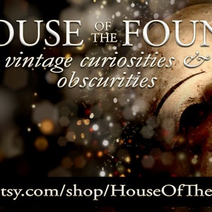 Op de afbeelding: Een vintage poppenhoofd met een gebarsten porseleinen masker, tegen een achtergrond van glinsterende lichten. De tekst "HOUSE OF THE FOUND vintage curiosities & obscurities" wordt boven het poppenhoofd weergegeven. De tekst "www.etsy.com/shop/HouseOfTheFound" wordt onder het poppenhoofd weergegeven.