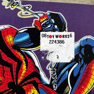 Puede incluir: Ilustraci&oacute;n de c&oacute;mic que presenta a Spider-Man en una pose din&aacute;mica. La obra de arte muestra el traje rojo y negro de Spider-Man con detalles de telara&ntilde;a, sobre un fondo p&uacute;rpura. Una pegatina con el texto "08 TOY WORKS 6 224386" es parcialmente visible.