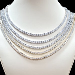 May include: A display of five different sized tennis chain necklaces with cubic zirconia stones. The necklaces are displayed on a white mannequin bust.