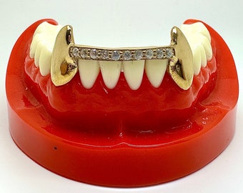 Puede incluir: Grill de oro con una fila de piedras de circonita cúbica transparentes. El grill se muestra en un modelo de boca de plástico rojo.