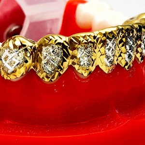 May include: Gold grill with diamond accents. The grill is made of gold and has a diamond pattern on the front. The grill is designed to fit over the front teeth.