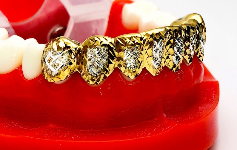 May include: Gold grill with diamond accents. The grill is made of gold and has a diamond pattern on the front. The grill is designed to fit over the front teeth.