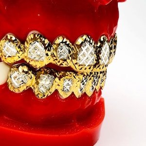 May include: A gold grill with diamond-shaped accents. The grill is made of gold and has a diamond-shaped pattern. The grill is on a red model of a mouth.